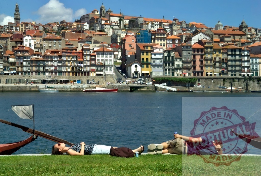 Couple relaxing on grass by Douro River, Porto cityscape | Couple resting on green grass bank along Douro River with historic Porto cityscape in background - Realized with Pictrs.com