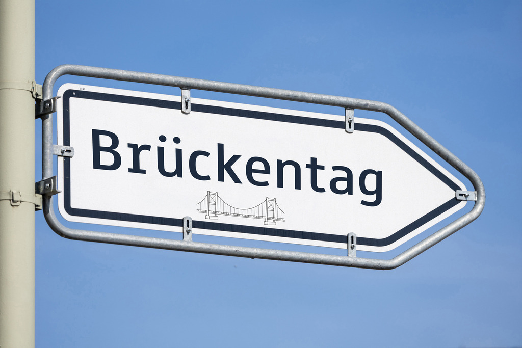 Brückentag nach Christi Himmelfahrt | (Fotomontage) Pfeilwegweiser mit Aufschrift BRÜCKENTAG und dem Symbol einer Brücke - Realisiert mit Pictrs.com
