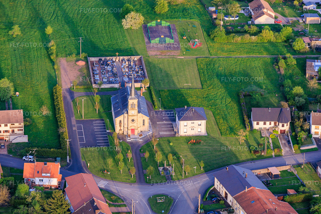 Aerial view: Church of Saint Joseph and Mairie of the West in Frémestroff in the state Moselle, France. – Photo: IMG_154357.jpg taken on 04/17/2026 by Werner Riehm/FLY-FOTO.com – Resolution of the original: 5574 x 3716 px