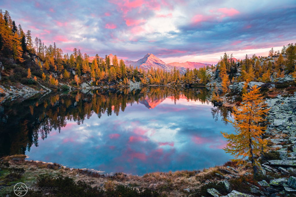 Morgen im Valle di Campo, TI | Herbststimmung in einem Tal im Tessin. Vom Sonnenaufgang erhellte Wolken spiegeln sich in einem Bergsee.Format 3 zu 2 - Realisiert mit Pictrs.com