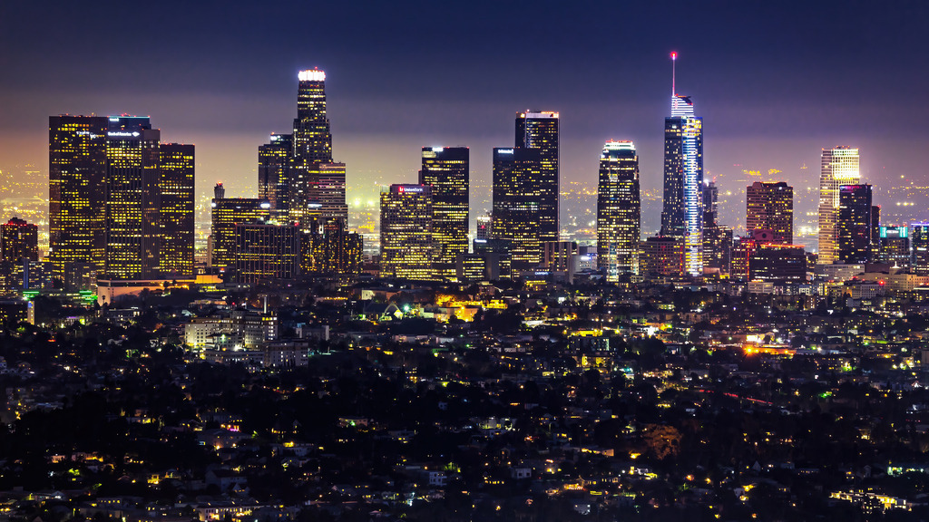 Wandbild - Das leuchtende Herz von Los Angeles | Dieses beeindruckende Bild zeigt die nächtliche Skyline von Los Angeles, die in einem funkelnden Lichtermeer erstrahlt. Die hohen Wolkenkratzer der Stadt leuchten in verschiedenen Farben und dominieren den nächtlichen Himmel. Die Stadt erstreckt sich weit, und die vielen Lichter der Straßen und Gebäude schaffen ein lebendiges und pulsierendes Ambiente. Der Kontrast zwischen den dunklen Silhouetten der Gebäude und den hellen Lichtern erzeugt eine dynamische und fesselnde Szene, die die Energie und das Leben der Stadt bei Nacht einfängt.