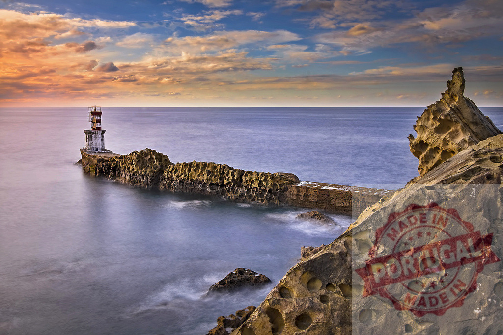 Lighthouse standing on a rocky cliff at sunset illuminating the ocean | Lighthouse on a rock formation in the sea at sunset creating a beautiful seascape - Realized with Pictrs.com