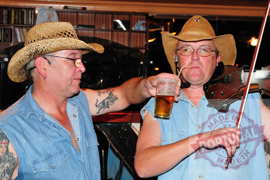 Country musicians playing violin and drinking beer | Two men wearing cowboy hats and denim shirts, one playing the violin and drinking beer - Realisiert mit Pictrs.com