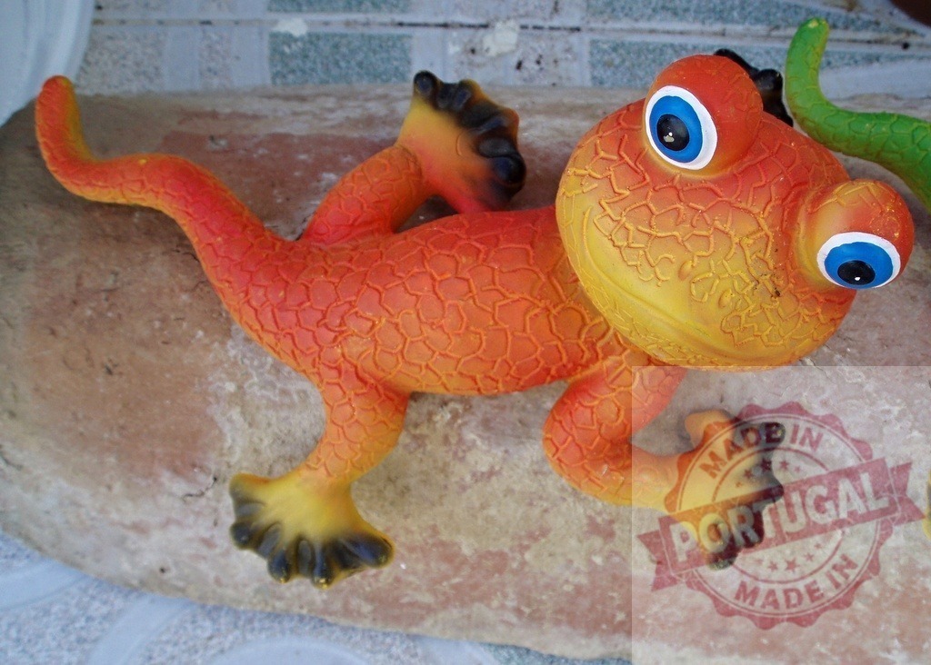 Orange reptile toy gecko creating garden decoration | Colorful toy gecko with big eyes resting on a rock, decorating an outdoor space - Realisiert mit Pictrs.com