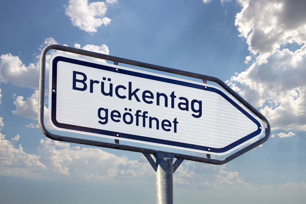 Schild BRÜCKENTAG GEÖFFNET | (Fotomontage) Richtungspfeil mit der Aufschrift BRÜCKENTAG GEÖFFNET vor blauem Himmel - Realisiert mit Pictrs.com
