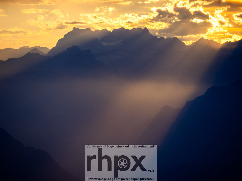 Lichtdurchflutete Gipfel | Licht. Weite. Magie.Dramatische Sonnenstrahlen durchbrechen die Wolkendecke und tauchen die gestaffelten Bergketten in ein atmosphärisches, goldenes Licht. Dieser Moment fängt die pure Erhabenheit der Alpen in einer einzigartigen Lichtstimmung ein.Wähle unter "Produktauswahl" dein Wunschformat: Vom klassischen Wandbild über Puzzle &amp; Tassen bis zum digitalen Download (z.B. als Handy-Hintergrund). - Realisiert mit Pictrs.com
