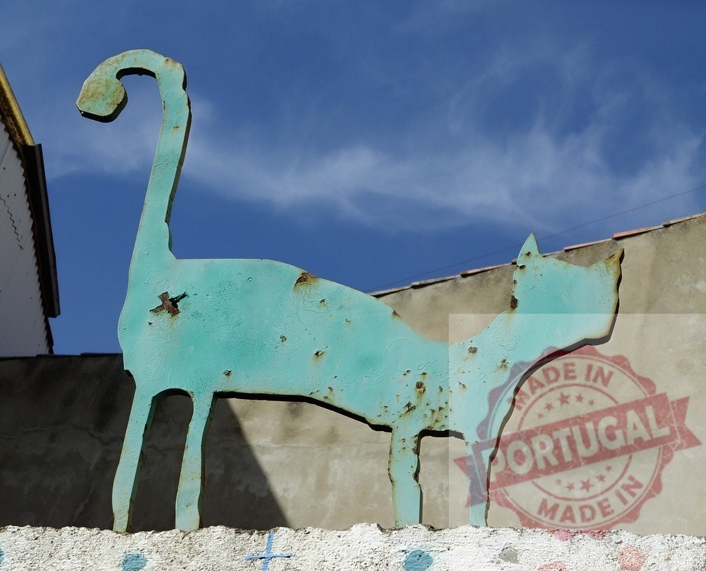 Rusty turquoise metal cat sculpture against blue sky | Rusty turquoise metal cat sculpture standing on a wall with a blue sky background - Realisiert mit Pictrs.com