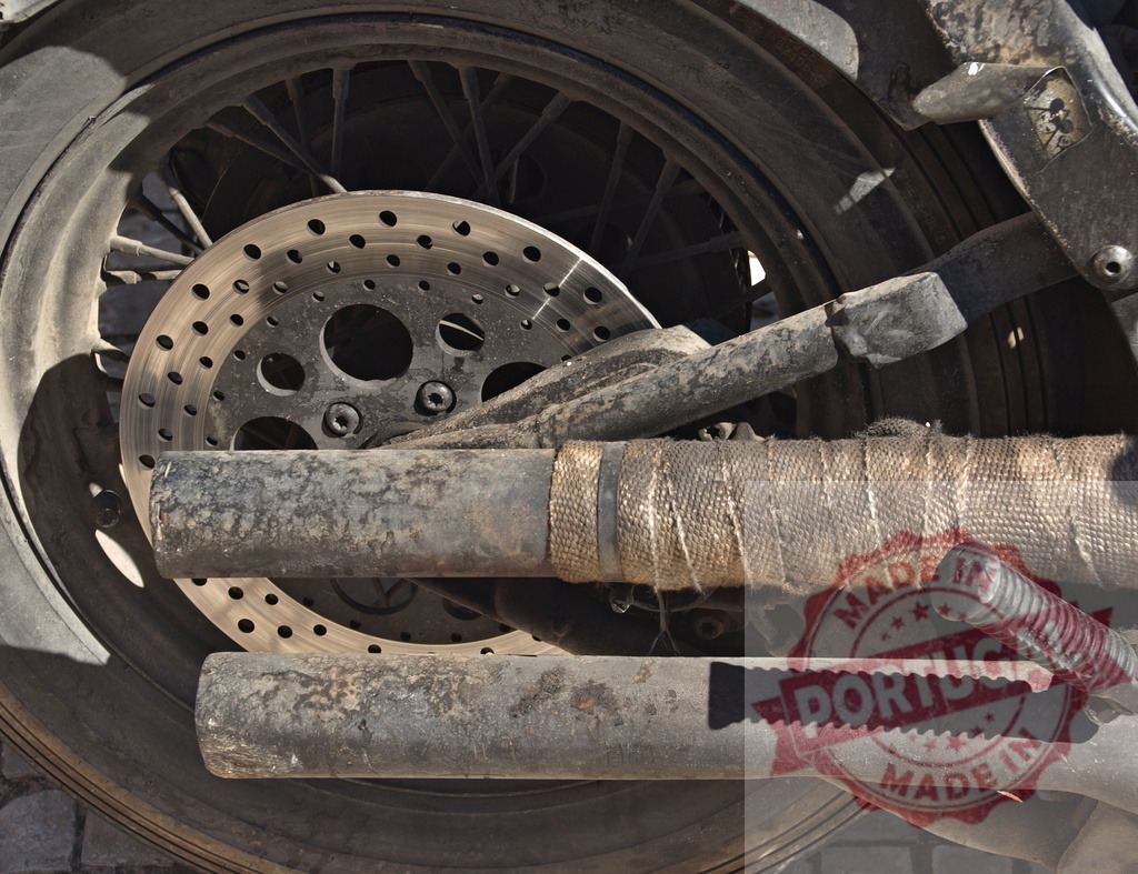 Vintage motorcycle wheel brake and exhaust pipes | Close up of a dirty old motorcycle wheel, brake disc, and exhaust pipes - Realized with Pictrs.com