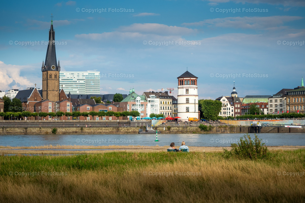 Paar vor der Düsseldorfer Altstadt am Rhein | Ein Paar sitzt vor dem Rhein mit der Düsseldorfer Altstadt. - Realisiert mit Pictrs.com
