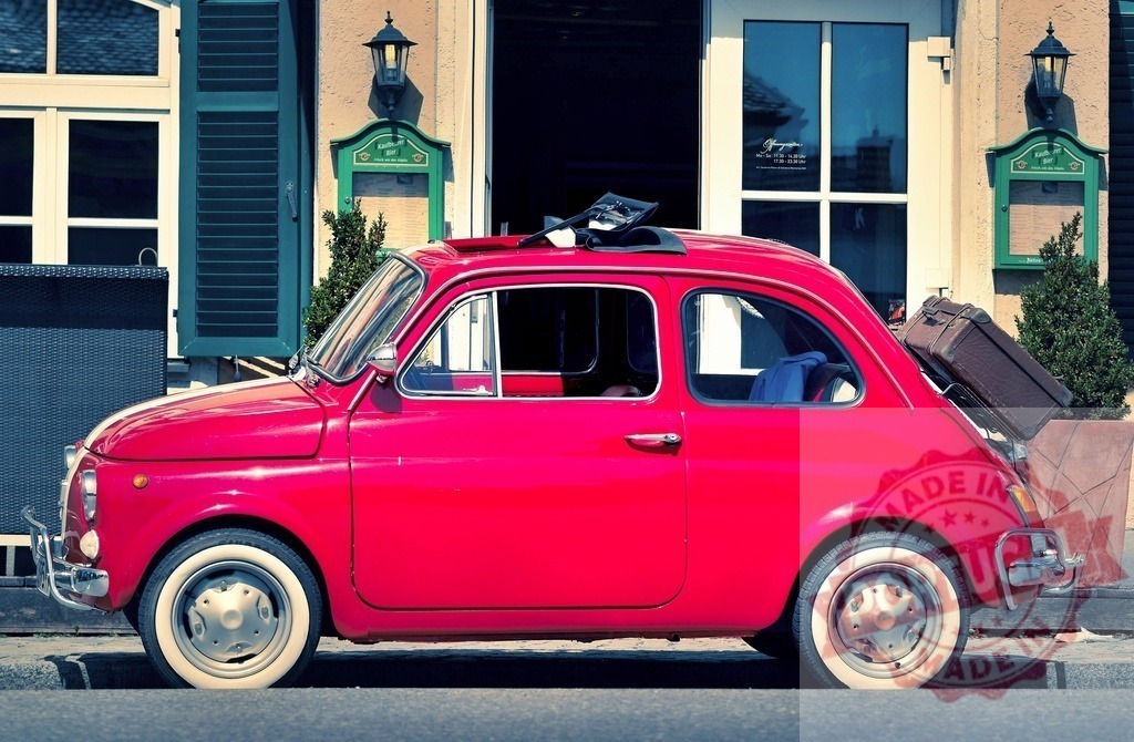 Red vintage Fiat 500 car traveling with luggage | Red vintage Fiat 500 car parked on a street with a suitcase in the back - Realized with Pictrs.com