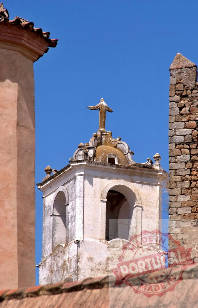Church bell tower with Jesus statue under blue sky. Spain - Extremadura | Old stone church bell tower with a statue of Jesus Christ against a clear blue sky - Realized with Pictrs.com
