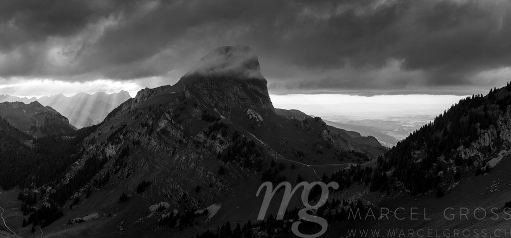 Dramatic Swiss Alps Landscape with Stockhorn from Laseberg | A panoramic view showcases a dramatic mountain landscape in the Swiss Alps. The scene features a rugged, green hillside leading to a towering peak partially obscured by clouds, creating a sense of scale and grandeur. The lighting suggests a cloudy summer day. - Realisiert mit Pictrs.com