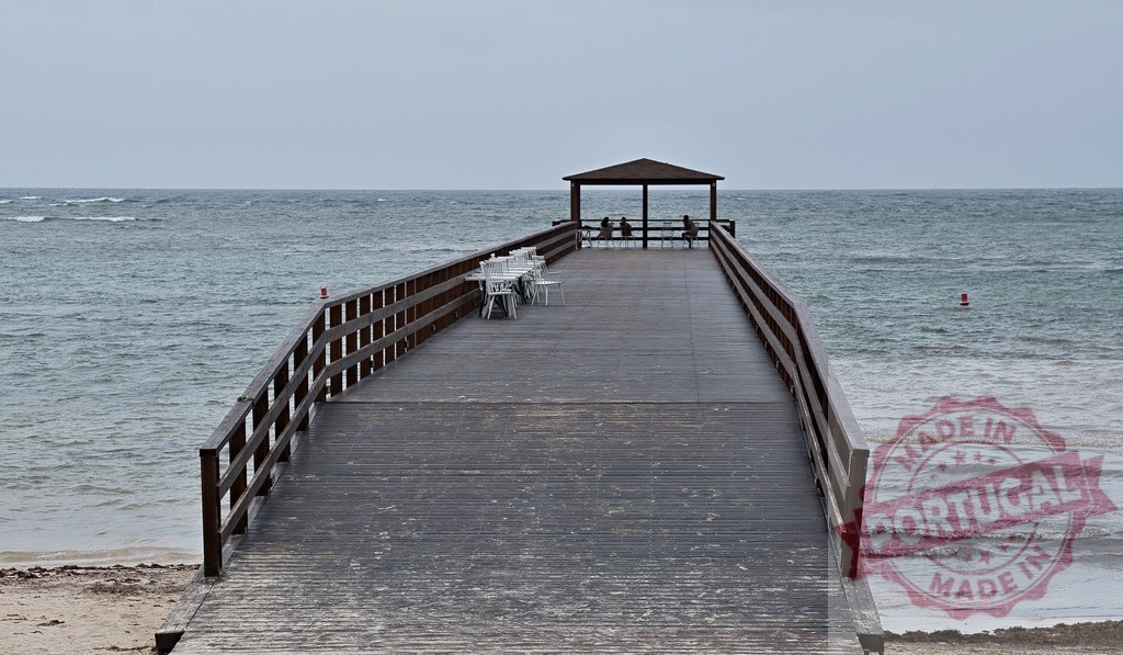Wooden pier with gazebo extending into ocean | People relaxing at the end of a long wooden pier with ocean view and cloudy sky - Realisiert mit Pictrs.com