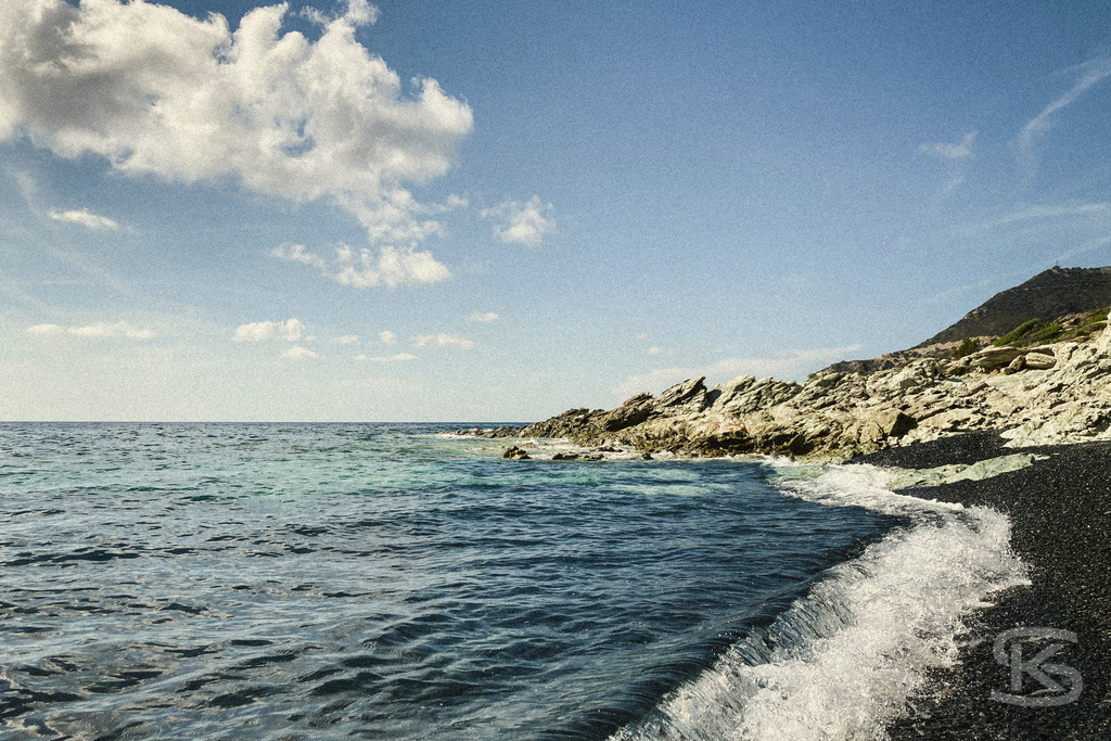 Idyllischer schwarzer Sandstrand auf Korsika mit kristallklarem Wasser und mediterraner Landschaft | Ein ruhiger, sonnenverwöhnter Sandstrand auf Korsika mit türkisblauem Meer, sanften Wellen und grüner Hügellandschaft im Hintergrund – perfekte Kulisse für einen entspannten Tag in der Natur. - Realisiert mit Pictrs.com