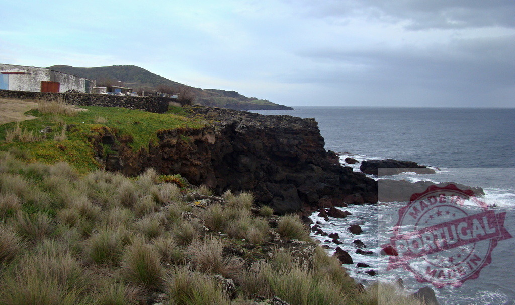 Rocky Atlantic volcanic coast in the Azores archipelago | Ocean waves crashing against dark volcanic rocks of an island cliff on a cloudy day - Realisiert mit Pictrs.com