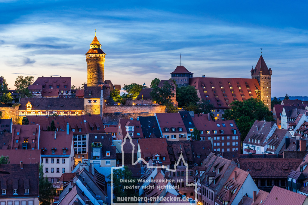 Nürnberger Stadtbild am Abend | Die Kaiserburg in Nürnberg bei Dämmerung mit dem beleuchteten Sinwellturm im Zentrum, einem der Wahrzeichen der Stadt. Die historischen Gebäude und die mächtigen Burgmauern erstrahlen im warmen Licht, während der Himmel in Blau- und Orangetönen den Übergang von Tag zu Nacht andeutet. - Realisiert mit Pictrs.com