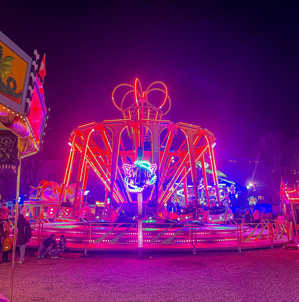 Basel Herbstmesse – Magisches Neon-Fahrgeschäft bei Nacht | High-End Fotokunst aus Basel: Ein faszinierendes, nächtliches Wandbild der Basler Herbstmesse. Das Zusammenspiel aus vibrierenden Neon-Farben in Pink und Violett und den dynamischen Lichtspuren des Fahrgeschäfts bringt moderne Urbanität und nostalgischen Jahrmarkt-Zauber an deine Wände. Perfekt als edler Blickfang auf Acrylglas, Leinwand oder Alu-Dibond. - Realisiert mit Pictrs.com