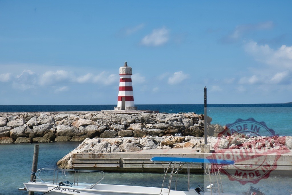 Red and white striped lighthouse standing on rocky jetty | Striped lighthouse marking the harbor entrance with a boat moored nearby - Realized with Pictrs.com