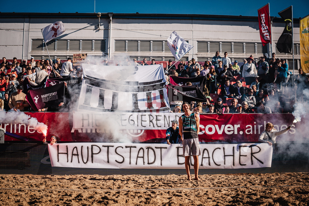 Beachvolleyball | Männer | Allianz German Beach Tour 2025 | Tourstop Berlin | 23.08.2025 | Einlauf von Jannik Kühlborn, im Hintergrund die Fangruppe Fraktion Bräune mit einer Choreo und Pyrotechnik, Hier Regieren Die Hauptstadt Beacher