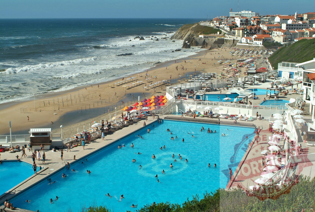 Praia das Maçãs beach pools and ocean during summer. Centro Portugal | People swimming in ocean pools and relaxing on beach umbrellas at a coastal resort - Realisiert mit Pictrs.com
