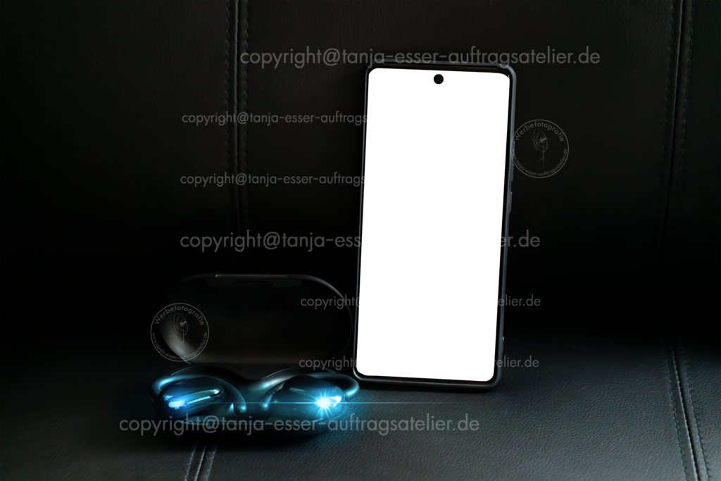 Modernes Smartphone mit Mockup Freisteller Display neben modernen Open Ear Sport Kopfhörern im Ladeetui | Modernes Smartphone mit Mockup Freisteller Display neben modernen Open Ear Sport Kopfhörern im Ladeetui mit LED-Licht auf schwarzem Lederhintergrund. Cyan farbiges Lens Flare.