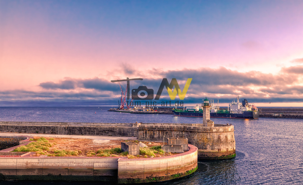 Im Hafen von Porto in abendlicher Stimmung-Sonnenuntergang | Das Bild zeigt einen Hafen bei Sonnenuntergang.Die Szene zeigt eine Mole oder einen Wellenbrecher im Vordergrund, der aus Stein und Beton gebaut ist.Im Hintergrund sind große Frachtschiffe im Hafenbereich sichtbar.Ein kleiner Leuchtturm steht auf dem Wellenbrecher. - Realisiert mit Pictrs.com