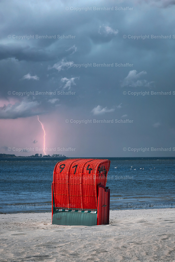 Gewitter am Strand | Ein roter Strandkorb an einem Sandstrand der Ostsee in der Kieler Förde während eines Gewitters mit Blitzeinschlag.  - Realisiert mit Pictrs.com