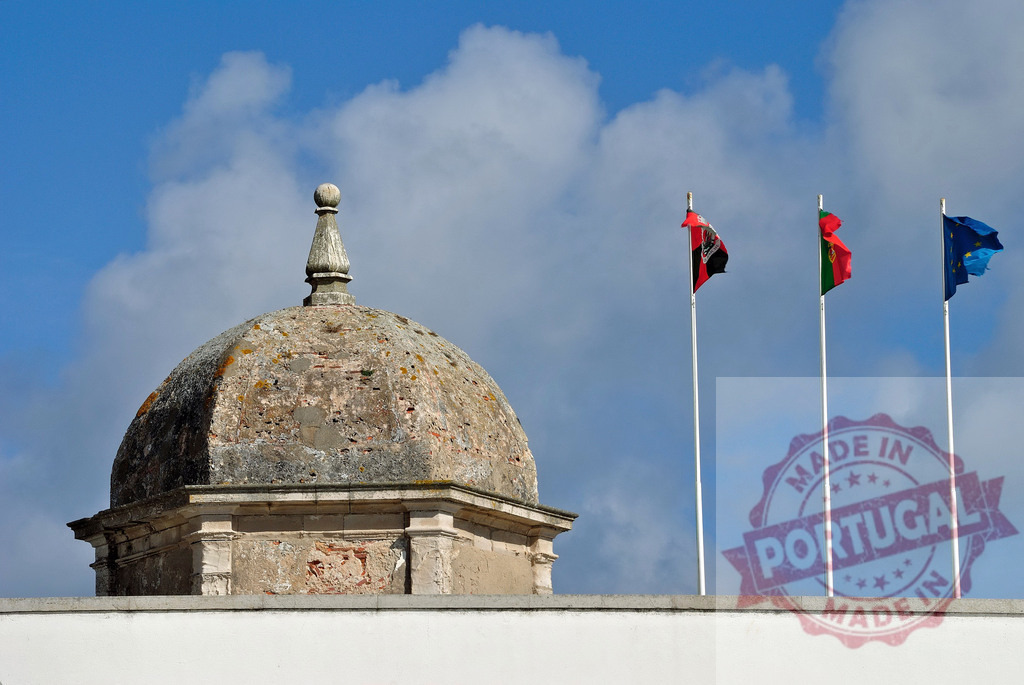 Historic dome structure with Portuguese and European Union flags swaying. Centro - Portugal | Old stone dome and flags against a blue sky, representing history, national identity, and European unity - Realisiert mit Pictrs.com