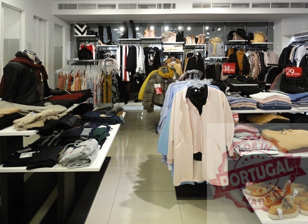 Clothing store interior filled with various apparel items | Clothing store interior showing garments on racks, tables, and shelves for retail shopping - Realized with Pictrs.com