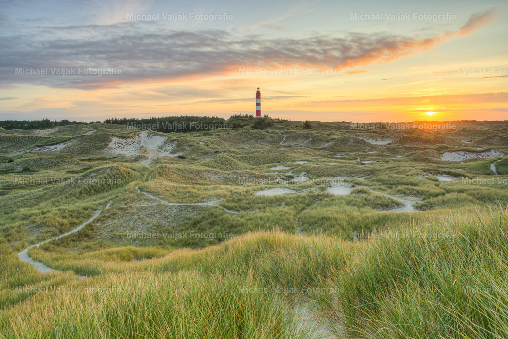 Leuchtturm auf Amrum bei Sonnenaufgang | Der Leuchtturm auf Amrum, bekannt als Amrumer Leuchtturm, ist ein markantes Wahrzeichen der Nordseeinsel. Bei Sonnenaufgang bietet er einen atemberaubenden Anblick, wenn die ersten Strahlen des Tages den Himmel in ein warmes Farbenspiel tauchen und das Meer in sanftes Licht hüllen. Dieses Schauspiel der Natur zieht jährlich zahlreiche Besucher an, die die ruhige Schönheit des Ortes und den malerischen Ausblick auf das Wattenmeer genießen möchten. - Realisiert mit Pictrs.com