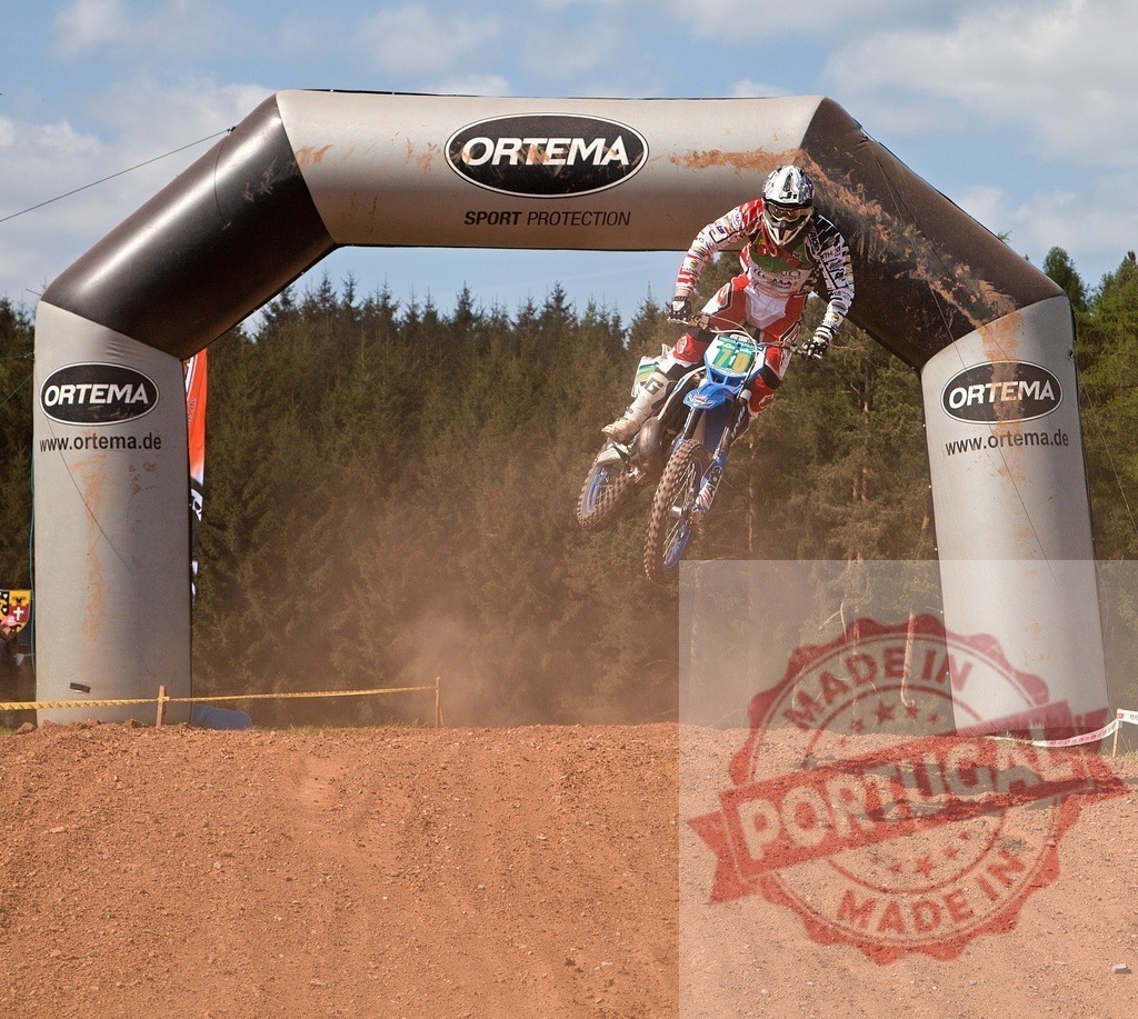 Motocross rider jumping dirt bike over finish line arch | Rider in full gear performing a jump on a dirt bike during a motocross race - Realized with Pictrs.com