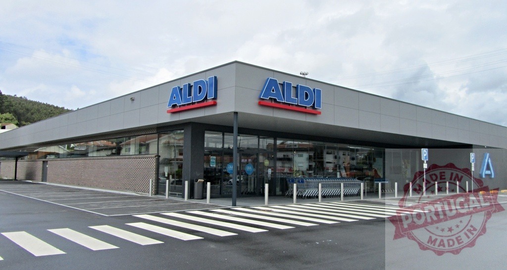 Aldi grocery store exterior and parking lot on a cloudy daytime | Aldi supermarket building exterior with parking lot and pedestrian crossing - Realized with Pictrs.com