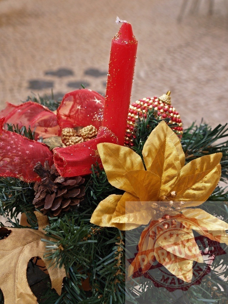 Red candle illuminating golden poinsettia flower in Christmas centerpiece | Christmas centerpiece with red candle, golden poinsettia, pine cone, bauble, and red ribbon, creating festive atmosphere - Realisiert mit Pictrs.com