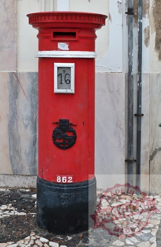 Classic red british mailbox standing on cobblestone street in Lisbon | Red british mailbox with white stripes and black base, number 16 and 862, standing on cobblestone street - Realized with Pictrs.com