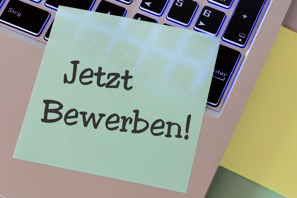 JETZT BEWERBEN Vorlage | Vorlage Mitarbeitersuche: Zettel mit der Aufschrift JETZT BEWERBEN auf einem Laptop  - Realisiert mit Pictrs.com