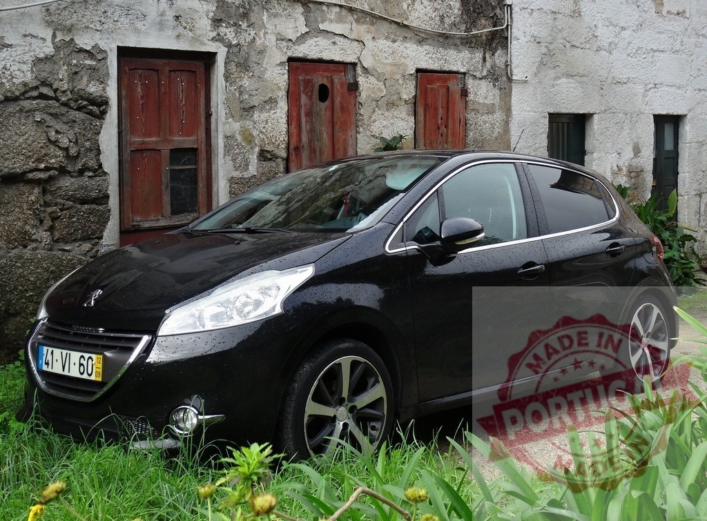 Peugeot 208 hatchback parked by old stone wall in Portugal | Black Peugeot 208 car parked in front of a rustic stone house with red doors - Realized with Pictrs.com