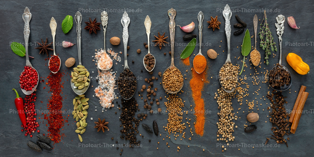 Exotische Gewürze und Kräuter auf dunkler Schieferplatte III | Diese professionelle Food-Fotografie zeigt eine beeindruckende Gewürzsammlung auf einer dunklen Schieferplatte. Elegante Silberlöffel enthalten verschiedene exotische Gewürze wie Kardamom, Koriander und Zimt. Frische rote Chilischoten, Knoblauchzehen und Walnüsse ergänzen die Komposition harmonisch. Die kunstvolle Anordnung der internationalen Gewürze und Kräuter schafft ein appetitliches Stillleben, das Kochbegeisterte und Gourmets gleichermaßen fasziniert. Jedes Detail unterstreicht die Vielfalt der kulinarischen Aromenwelt perfekt. - Realisiert mit Pictrs.com