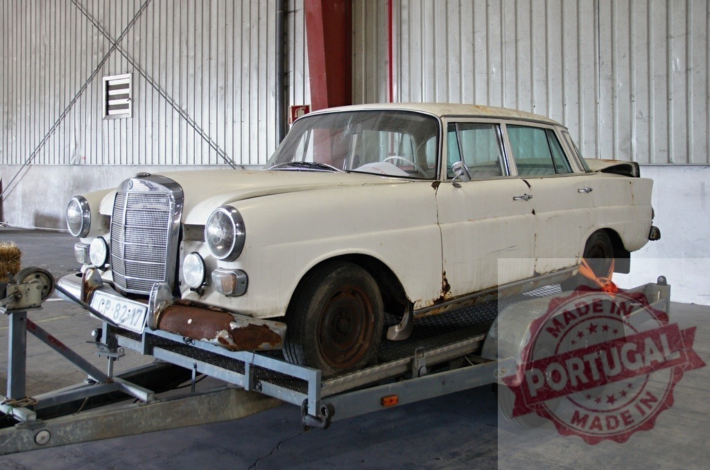 Rusty Mercedes-Benz 220S being transported on a trailer | Abandoned Mercedes-Benz 220S with rust spots being transported on a trailer inside a warehouse - Realized with Pictrs.com