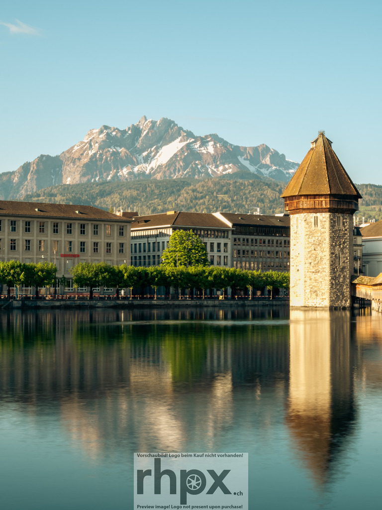 Kapellbrücke und Pilatus im Morgenlicht, Luzern | Die Kapellbrücke mit dem Wasserturm spiegelt sich ruhig in der Reuss, während im Hintergrund der Pilatus im klaren Morgenlicht erscheint. Klassische Luzerner Ansicht mit sauberer Linienführung, warmem Licht und ruhiger Wasseroberfläche – ein zeitloses Postkartenmotiv mit alpinem Bezug. - Realisiert mit Pictrs.com