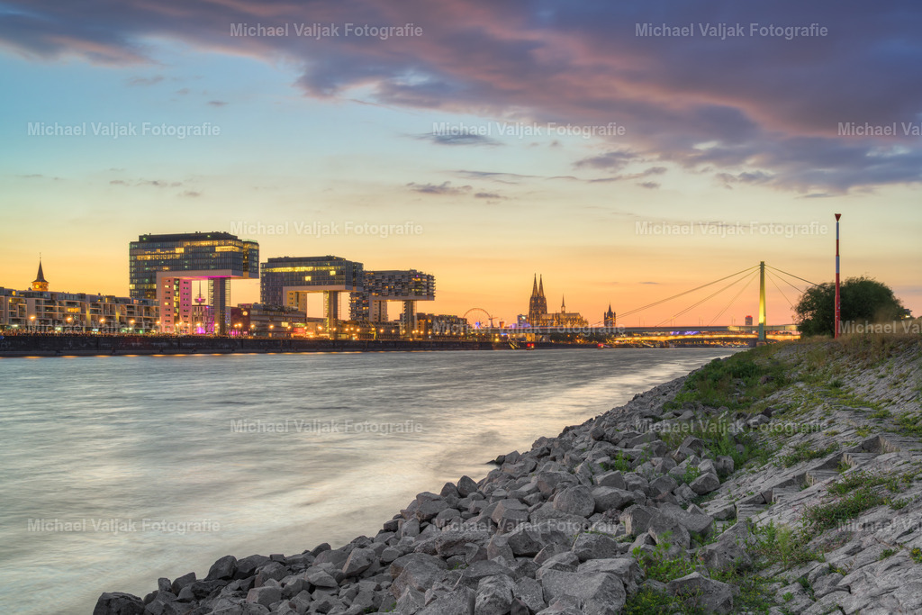 Abends am Rheinufer bei den Poller Wiesen | Am späten Abend liegt eine ruhige und stimmungsvolle Atmosphäre über den Poller Wiesen am Rhein. Der Himmel ist bereits deutlich dunkler, während die Beleuchtung auf der gegenüberliegenden Rheinseite und in der Kölner Stadtkulisse bereits eingeschaltet ist.Die weite Uferlandschaft der Poller Wiesen bei Niedrigwasser bildet einen natürlichen Kontrast zur beleuchteten Stadt. Im Hintergrund prägen die Kölner Architektur und die charakteristische Silhouette der Domstadt das Bild und verleihen der Aufnahme ihren unverwechselbaren urbanen Charakter.Ein atmosphärisches Abendfoto von Köln am Rhein, das die besondere Stimmung der Stadt in den späten Abendstunden zwischen natürlicher Landschaft und urbaner Beleuchtung einfängt. - Realisiert mit Pictrs.com