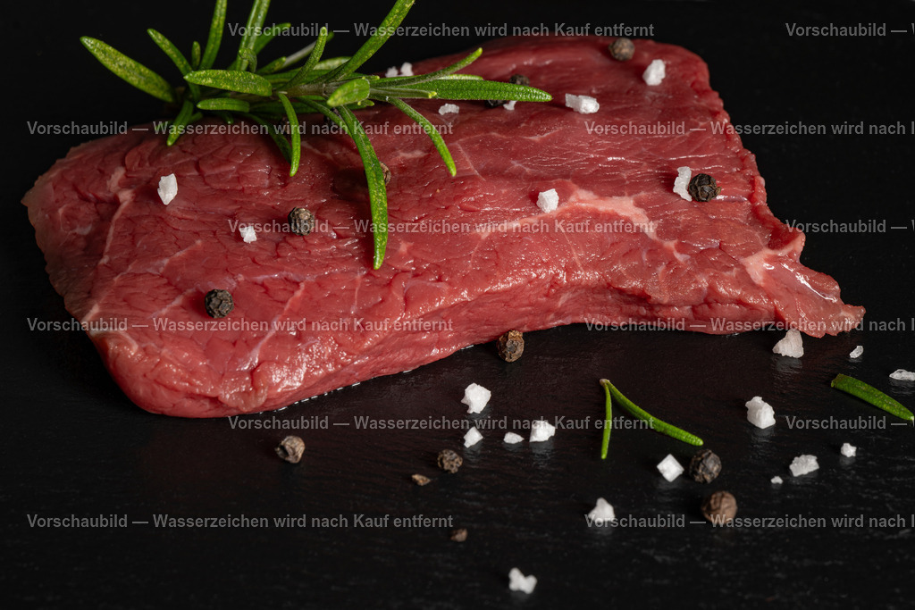 rohes Rinder Hüftsteak auf schwarzer Schieferplatte angerichtet | rohes Rinder Hüftsteak auf schwarzer Schieferplatte angerichtet. Dekoriert mt einen Zweig Rosmarien, Pfefferkörnern und groben Salz - Realisiert mit Pictrs.com