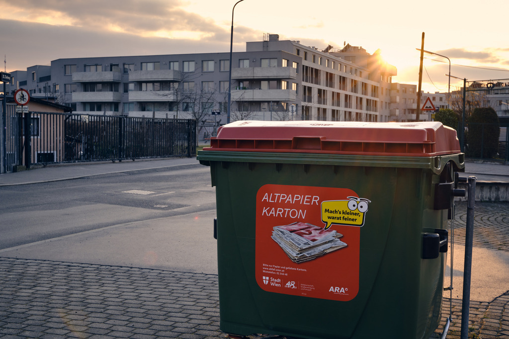 Altpapiercontainer an einer Strassenecke | Wien, Austria - February 28, 2023: Altpapiercontainer an einer Strassenecke, dahinter ist eine Wohnanlage. - Realisiert mit Pictrs.com