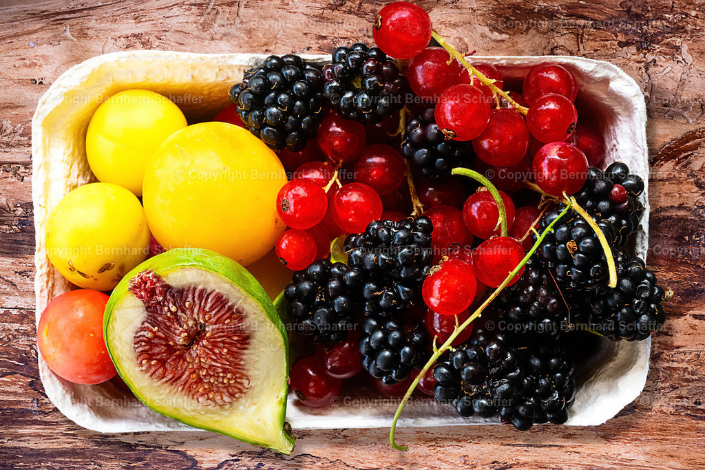 Obstschale mit Vitaminen | Eine Obstschale aus Karton mit Aprikosen, Feige, Johannisbeeren und Brombeeren steht auf einem Holztisch. - Realisiert mit Pictrs.com