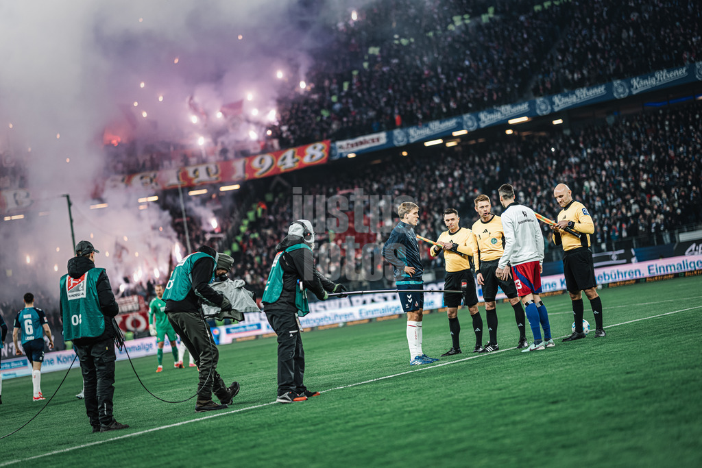 Fußball | Männer | Saison 2024/2025 | 2. Fußball-Bundesliga | 18. Spieltag | Hamburger SV vs. 1. FC Köln | 18.01.2025 | v.l. Timo Hübers (#4, 1. FC Köln) und Jonas Meffert (#23, HSV) beim Münzwurf, im Hintergrund der Gästeblock aus Köln mit Pyrotechnik