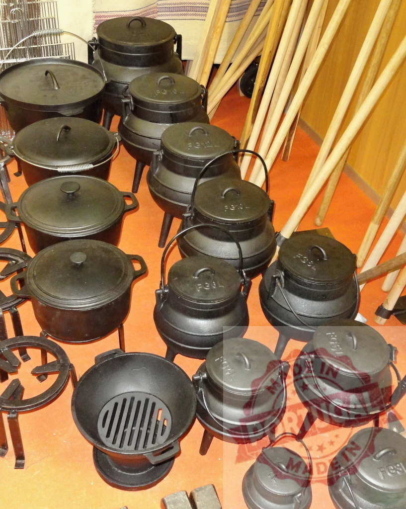 Cast iron potjiekos pots on display | Various traditional cast iron potjiekos cooking pots and accessories on an orange floor - Realisiert mit Pictrs.com