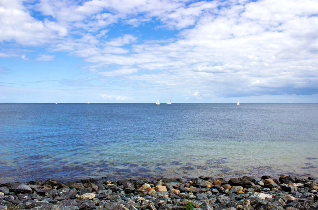 Wandbilder: Strand in Schönhagen | Dieses Wandbild im Querformat zeigt die Ostsee in Schönhagen. Dieser mit Steine befestigte Uferbereich befindet sich zwischen dem Sandstrand und der Steilküste. Am blauen Himmel sind helle Wolken zu sehen.  - Realisiert mit Pictrs.com