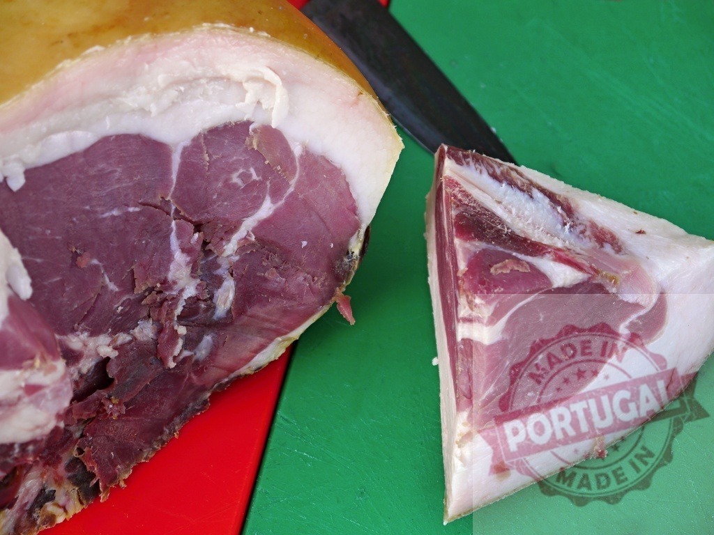 Slicing cured ham leg on cutting board with knife | Cured ham with a knife and sliced piece resting on a green chopping board - Realisiert mit Pictrs.com