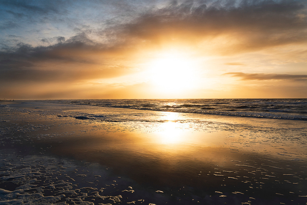 Goldenes Leuchten – St. Peter-Ording | Ein friedlicher Winterabend an der Nordseeküste: Die untergehende Sonne färbt Himmel und Wasser in warme Gold- und Orangetöne, während die Wellen sanft über den spiegelglatten Sand rollen. Ein Bild, das Ruhe ausstrahlt und zum Träumen einlädt. - Realisiert mit Pictrs.com