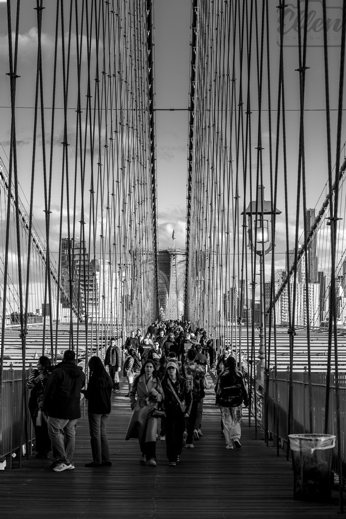 Crossing Lines | Life unfolds along the iconic span of the Brooklyn Bridge — a meeting of rhythm, geometry, and humanity. Between steel cables and city light, New York’s heartbeat moves in graceful patterns of connection. - Realisiert mit Pictrs.com