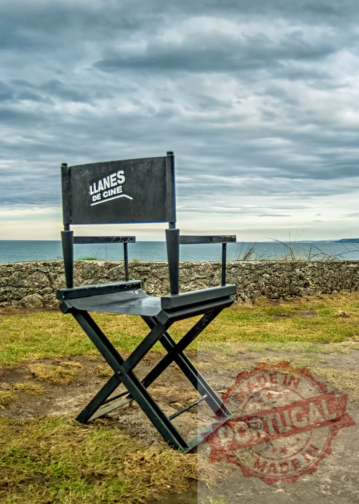 Director chair overlooking the Cantabrian Sea in Llanes, Asturias | Black director chair with the inscription Llanes de cine facing the Cantabrian Sea under a cloudy sky - Realized with Pictrs.com